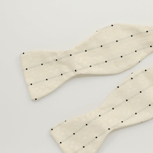 Cream bow tie with black dots on a light gray background