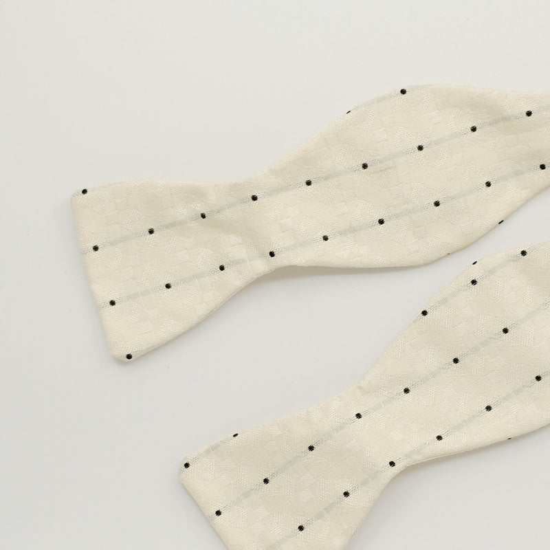 Cream bow tie with black dots on a light gray background