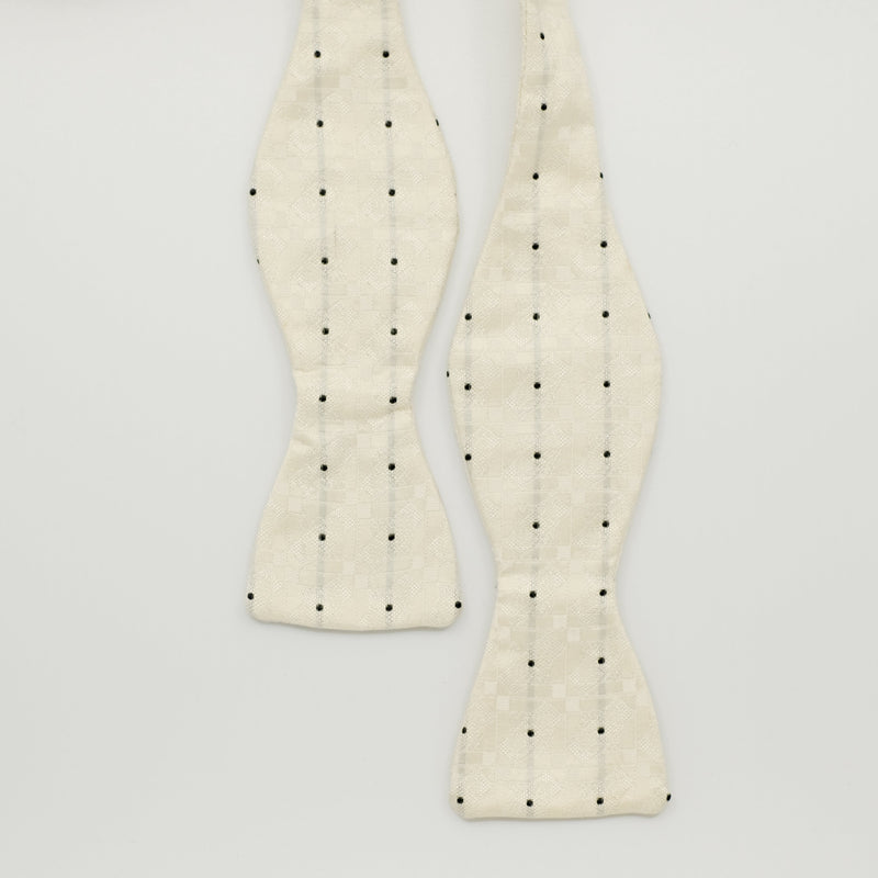 White bow tie with black polka dots on a light gray background